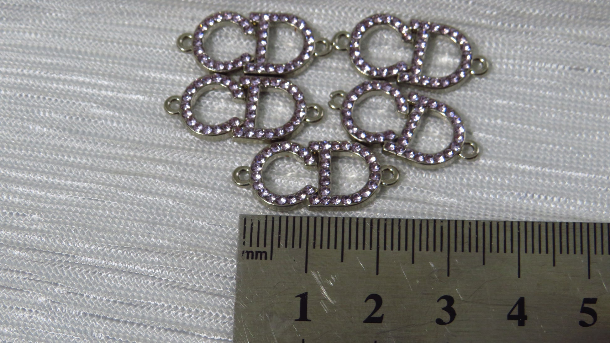 Silver jewelry components with purple stones on a white fabric background, measured against a ruler.