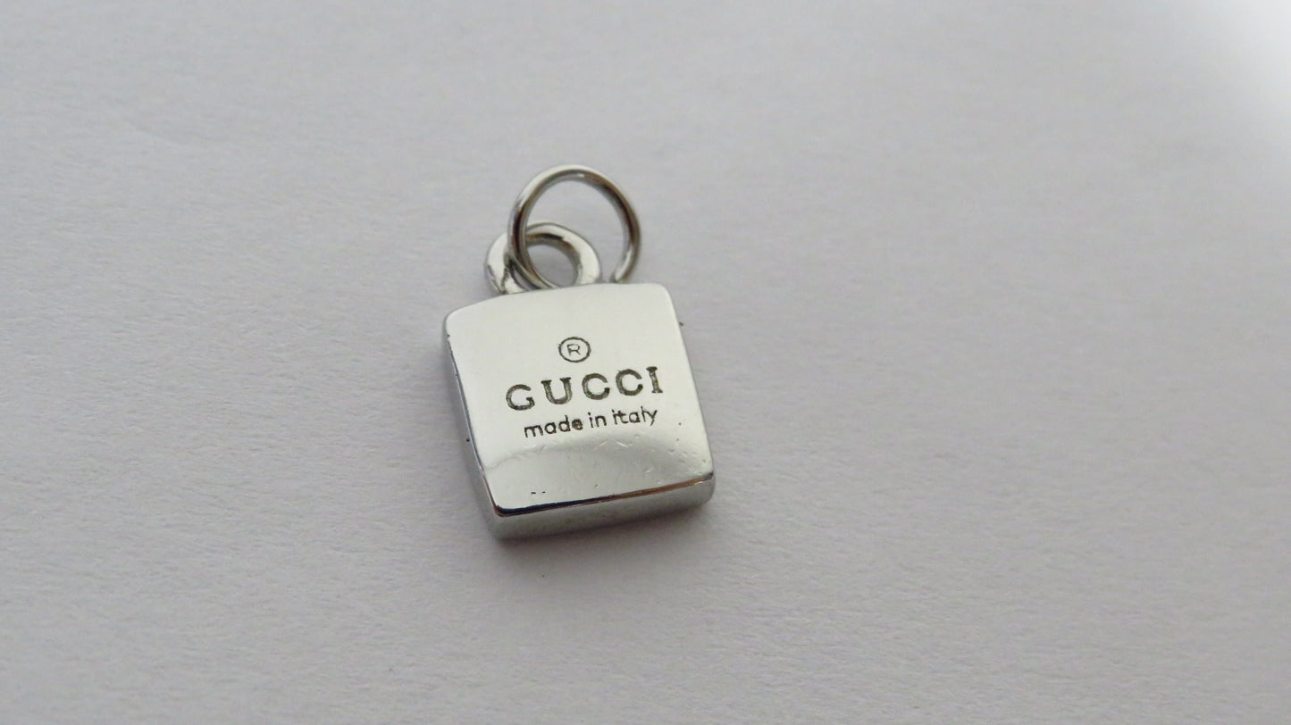 Silver Gucci charm on a gray background