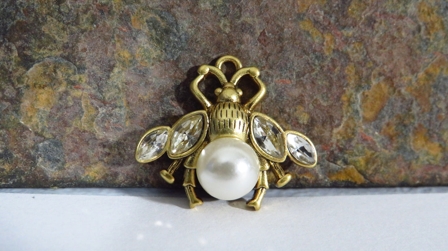 Gold bee-shaped brooch with pearl body on a textured stone background