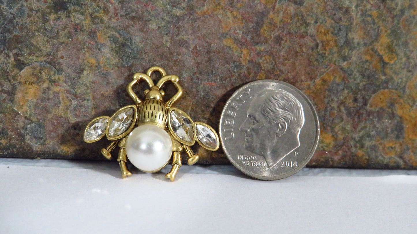 Gold bee-shaped brooch with pearls next to a quarter on a textured surface