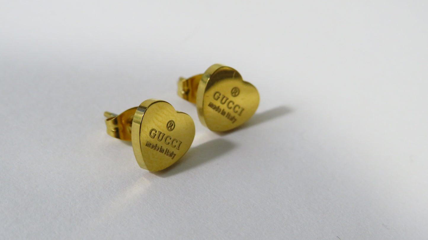 Gold heart-shaped Gucci earrings on a light gray background