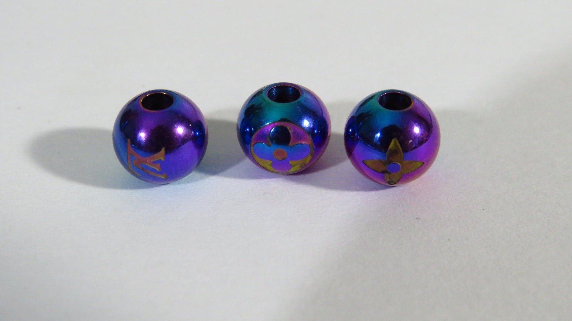 Three metallic purple beads with star designs on a white background
