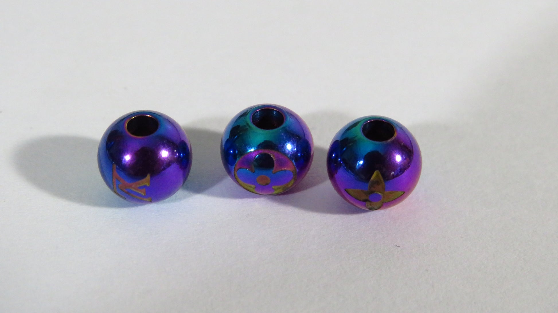 Three metallic beads with a colorful, iridescent finish on a white background