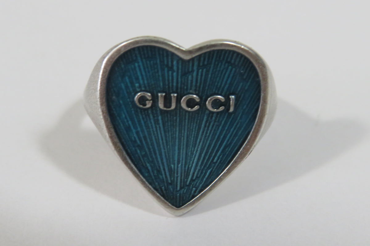 A Gucci heart-shaped ring with a textured blue enamel face and a silver-tone metal border, shown on a plain light gray background.