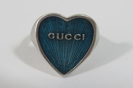A Gucci heart-shaped ring with a textured blue enamel face and a silver-tone metal border, shown on a plain light gray background.